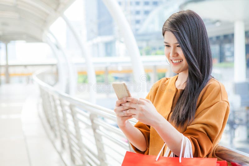 Woman use of mobile phone and carrying paper bags in city .