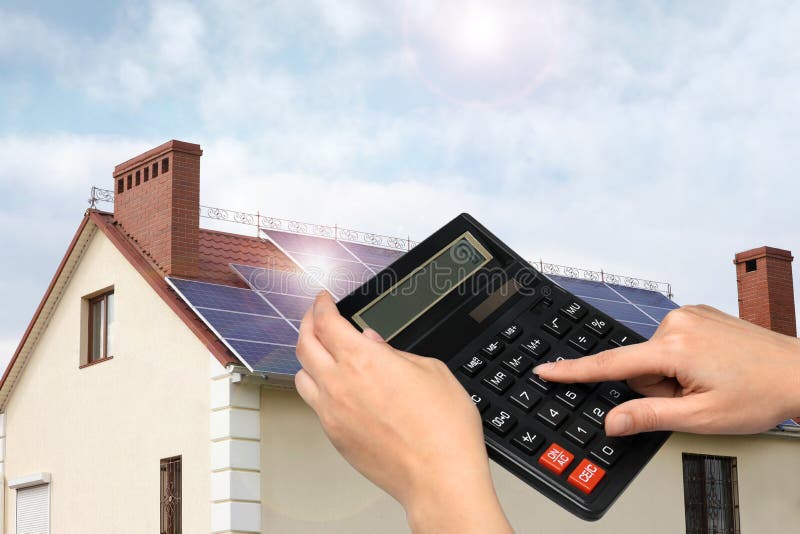 Woman using calculator against house with solar panels. Renewable energy and money saving