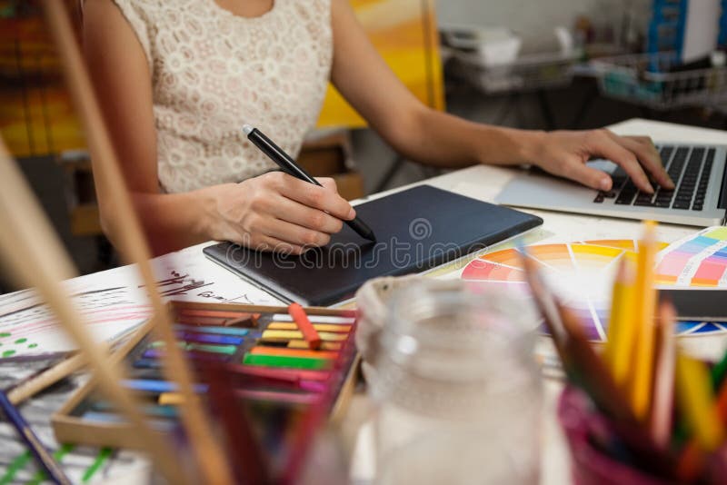 Mid-section of woman using graphic tablet and laptop in drawing class