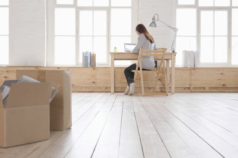 Woman Using Laptop At Desk In Loft Apartment