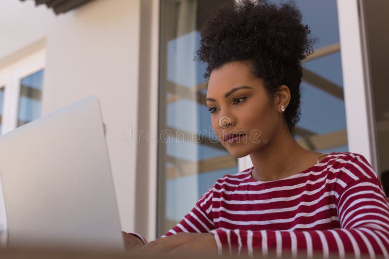 Front view of a beautiful African American woman using her laptop on her terrace at home. Front view of a beautiful African American woman using her laptop on her terrace at home