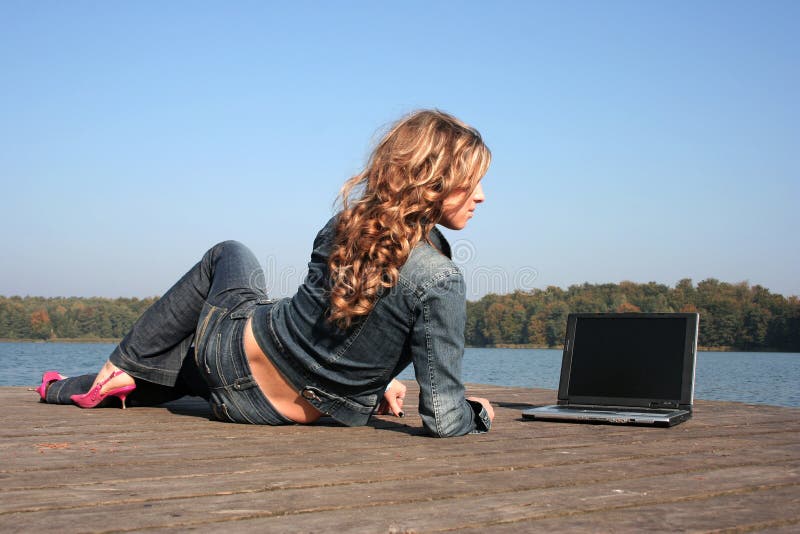 Woman using laptop by lake