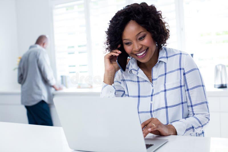 Woman using laptop while talking on mobile phone