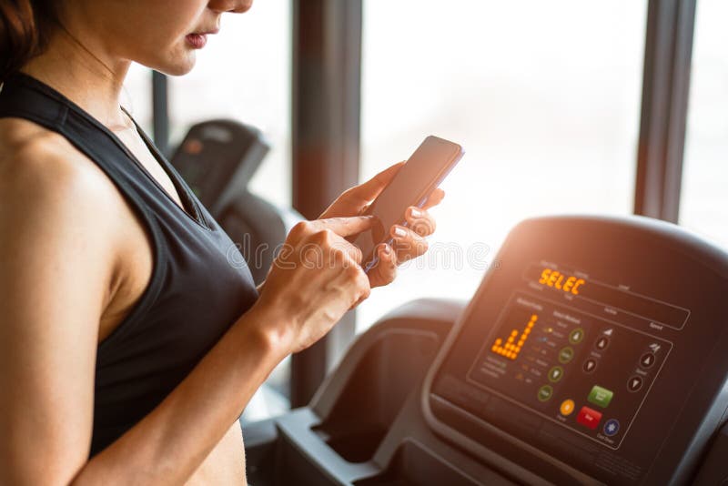 Woman using smart phone when workout or strength training at fitness gym on treadmill. Relax and Technology concept. Sports stock photos Woman using smart phone when workout or strength training at fitness gym on treadmill. Relax and Technology concept. Sports stock photos