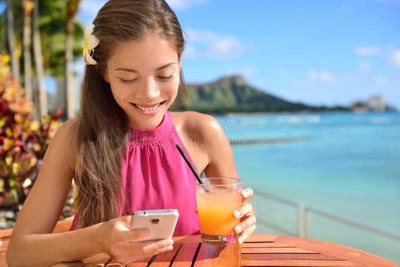 Woman using smartphone at beach bar having a drink