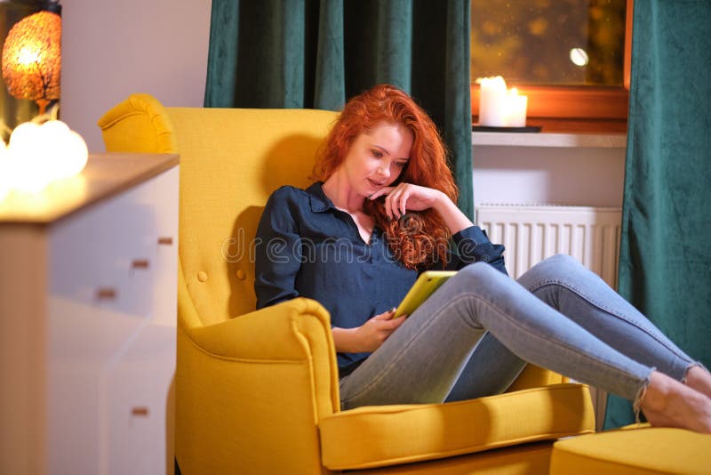 Woman  using a tablet on line at home sitting on a yellow in the living room at home . Covid isolation