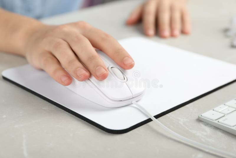 Woman using wired computer mouse on pad at light grey marble table, closeup