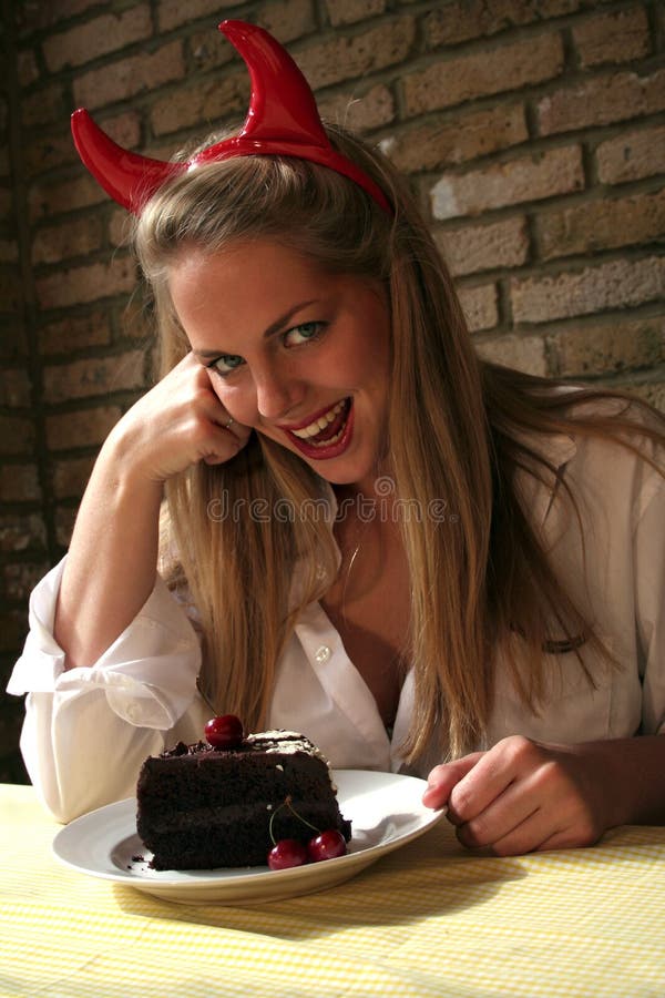 Immagine di una donna bionda, con corna da diavolo tentato da una ciliegia, torta al cioccolato, concettuale tentazione.