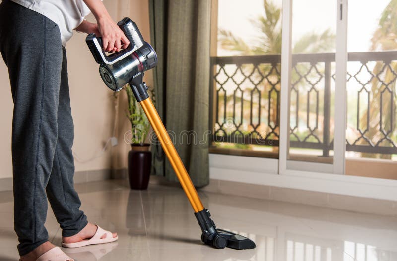 Woman vacuuming the living room with cordless vacuum cleaner