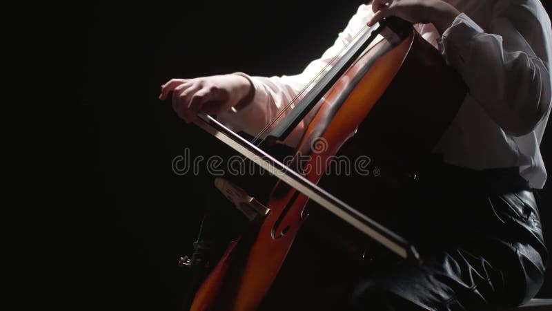 Woman virtuoso musician playing classical melody on strings cello in studio, black background, side view. Musician plays stock video footage
