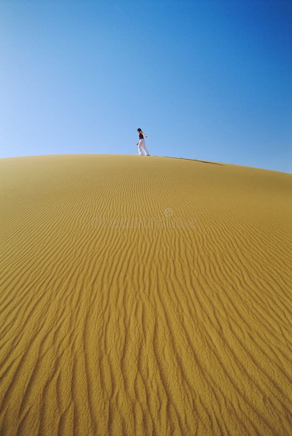 Woman walking across desert sand dune