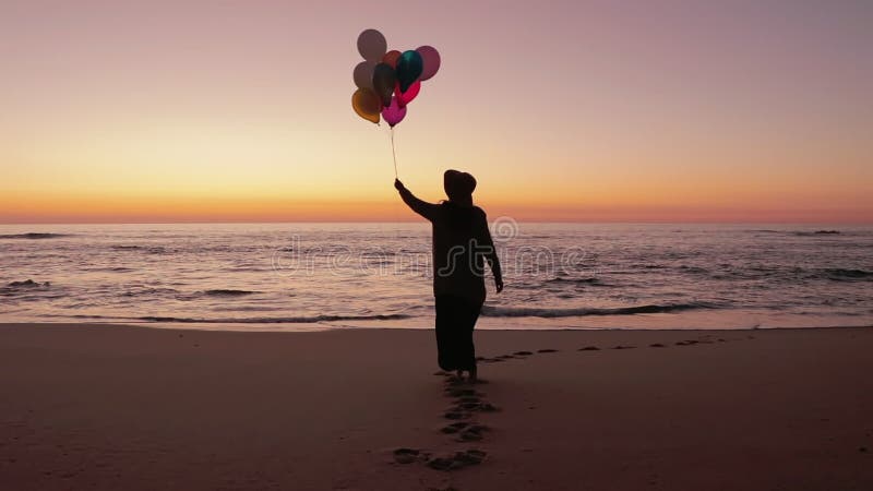 Woman walking on the beach with balloons