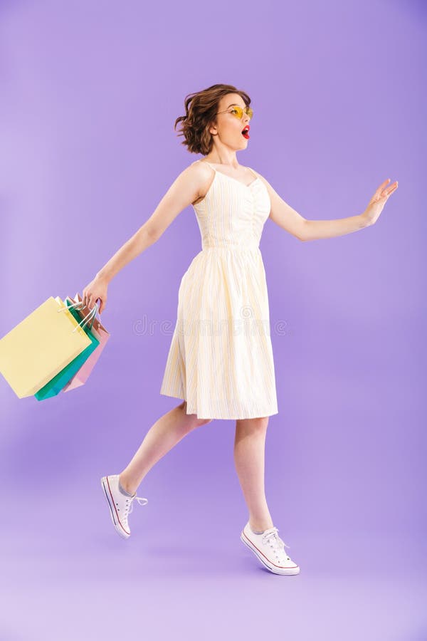 Woman walking isolated over purple wall background holding shopping bags.