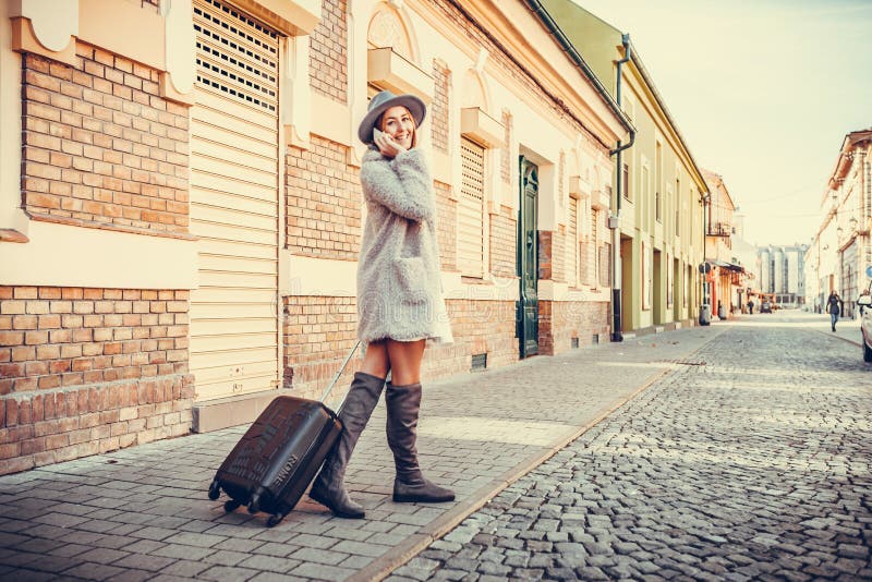 Woman walking through the street with suitcase while talking on