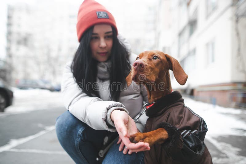 Woman in Warm Clothes Sits on the Ground with a Puppy on the Background ...