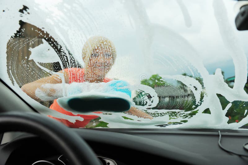 A young blonde woman washes her car