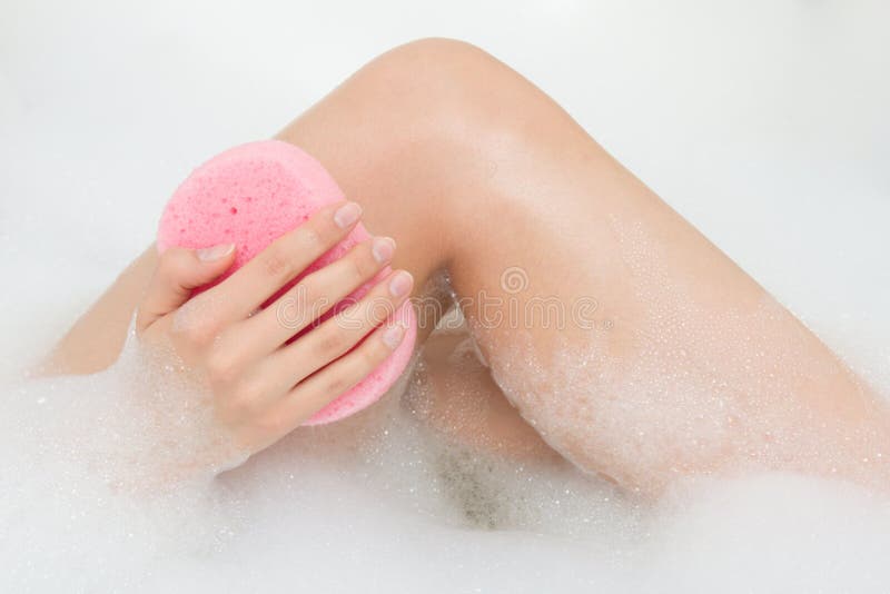 Woman washing legs in bath with sponge