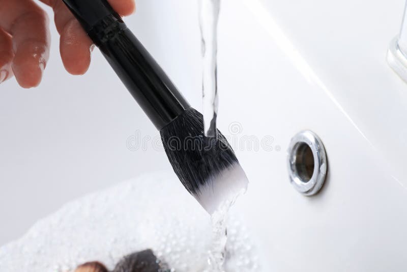 Woman washing makeup brush under stream of water in sink, closeup