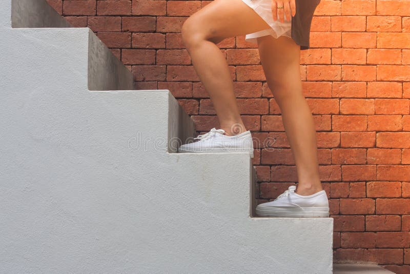 Woman wear black t-shirt and white shorts , her is walking up concrete stairs outside the buildings with red brick wall background