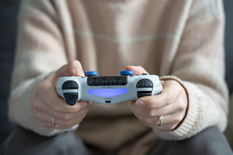 Woman, wearing casual comfortable clothes, sitting on the sofa and playing video games with wireless controller