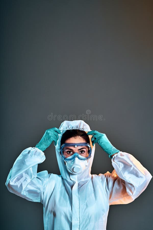 Woman wearing gloves, biohazard protective suit, eyeglasses and mask. For corona virus or Covid-19 protection. Vertical photo. Grey background. Copy space