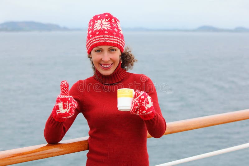 Woman wearing in hat and mittens holds cup of tea