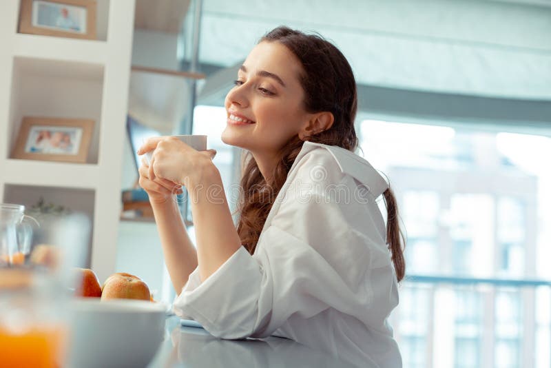 Woman wearing white shirt feeling relaxed drinking coffee stock photo Woman wearing white shirt feeling relaxed drinking coffee stock photo