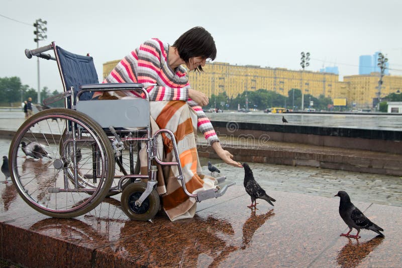 Žena na vozíku kŕmi holuby v ulici mestách.
