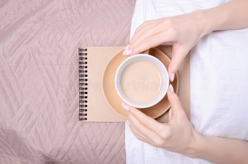Woman in the white bed cup of coffee in hand notebook stock photo