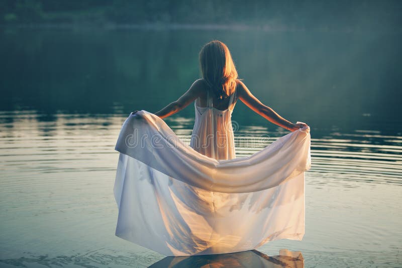 Woman with white dress in a lake at sunset