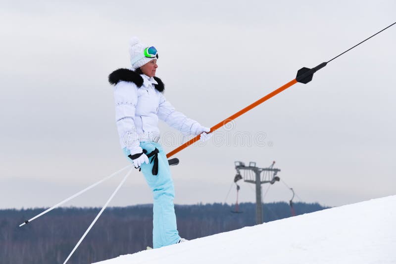 A woman skiing a mountain resort on a ski lift. Pull, hillside.