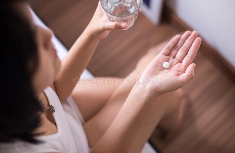 Woman with white pill painkillers on hand and a glass of water