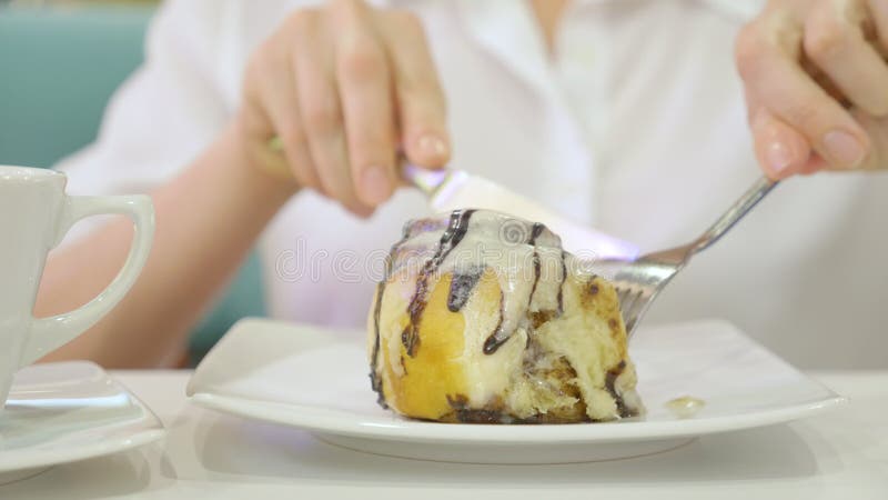 A woman in a white shirt eats with a knife and fork a bun cinnamon roll in a cafe and drinks coffee. Breakfast concept. stock image A woman in a white shirt eats with a knife and fork a bun cinnamon roll in a cafe and drinks coffee. Breakfast concept. stock image