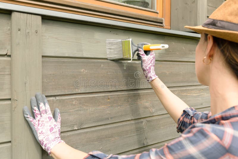 Woman worker painting wooden house exterior wall with paintbrush and wood protective color stock photo Woman worker painting wooden house exterior wall with paintbrush and wood protective color stock photo