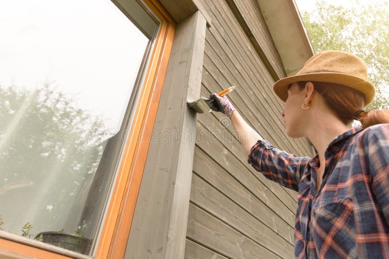 Woman worker painting wooden house exterior wall with paintbrush and wood protective color royalty free stock image Woman worker painting wooden house exterior wall with paintbrush and wood protective color royalty free stock image