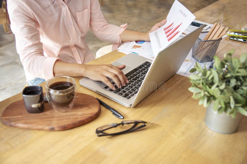 Woman working at home office desk using laptop business financial document chart and graph on wooden table with coffee cup. Woman