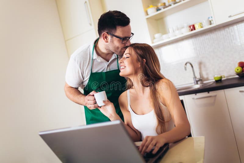 Woman working on laptop in kitchen as boyfriend prepares meal royalty free stock photos Woman working on laptop in kitchen as boyfriend prepares meal royalty free stock photos
