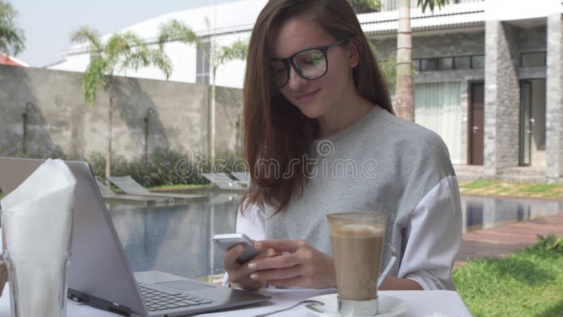 Woman working on laptop and take smartphone near pool on tropical luxury villa . Female work on computer and mobile