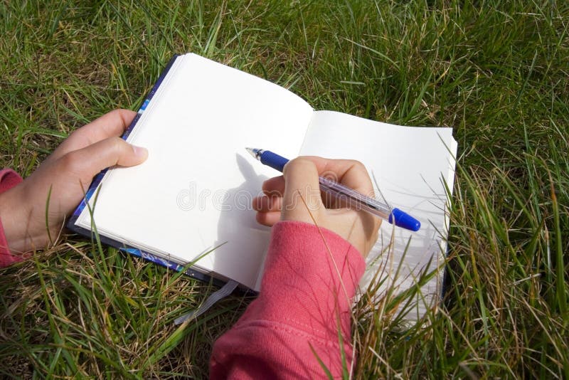 Woman lying in the grass and writing in a blank book. Woman lying in the grass and writing in a blank book