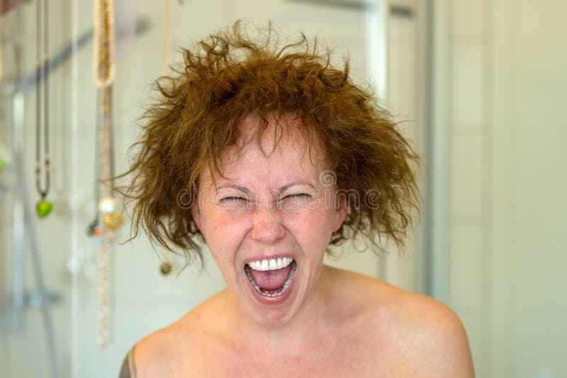 Woman yelling in frustration on a bad hair day with her unmanageable curly hair flying in all directions after showering in a close up portrait