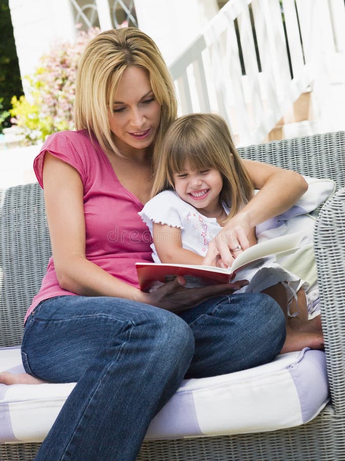 Woman and young girl sitting on patio reading book