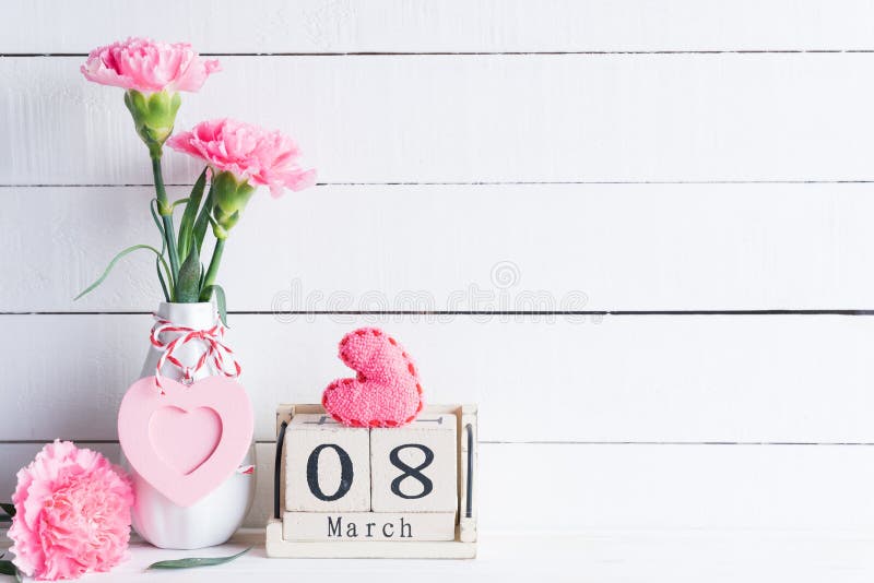 Womans day concept. Pink carnation flower in vase and red heart with March 8 text on wooden block calendar on white wooden stock images Womans day concept. Pink carnation flower in vase and red heart with March 8 text on wooden block calendar on white wooden stock images