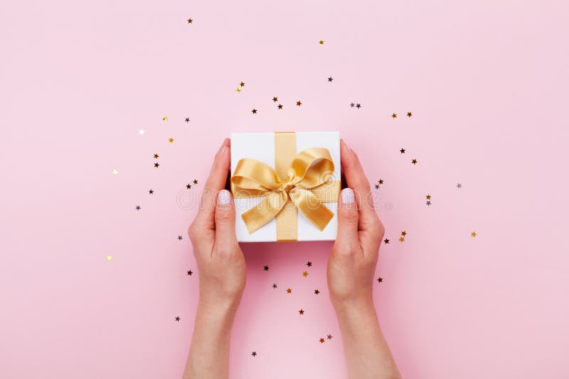 Womans hands holding gift or present box decorated confetti on pink pastel table top view. Flat lay composition for birthday. royalty free stock photo