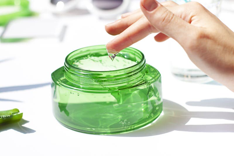 Womas hand is dipping finger in a cosmetic aloe vera gel in a transparent jar close up.