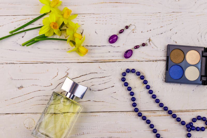 Women accessories on white wooden background. Bottle of perfume, eye shadow, necklace, earrings and yellow daffodils stock photos Women accessories on white wooden background. Bottle of perfume, eye shadow, necklace, earrings and yellow daffodils stock photos