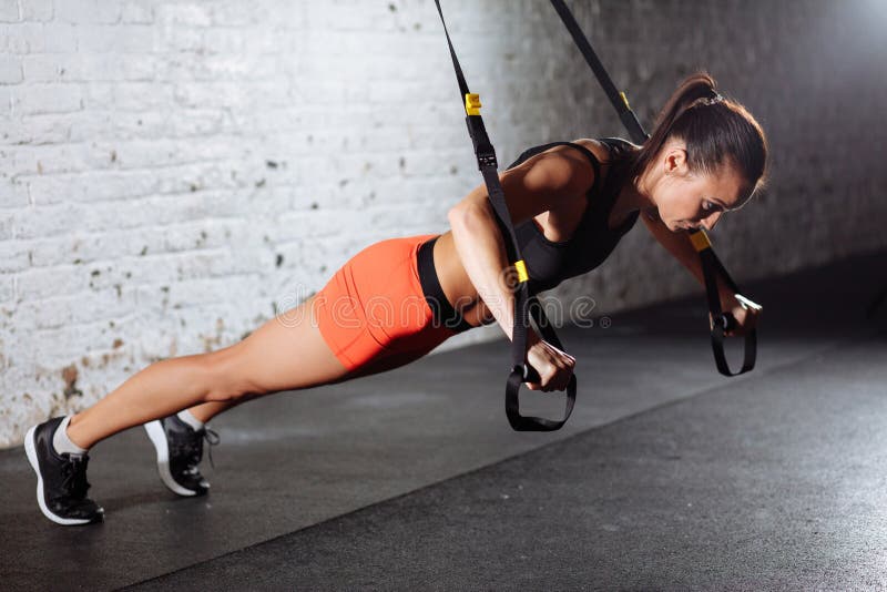 Women training arms with trx fitness straps in the gym doing push
