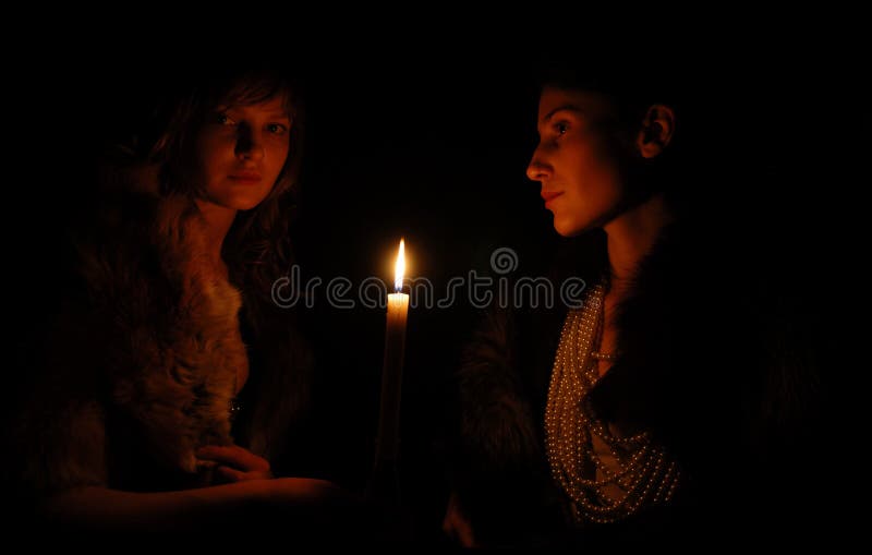 Women on each side of candle in the dark stock photos