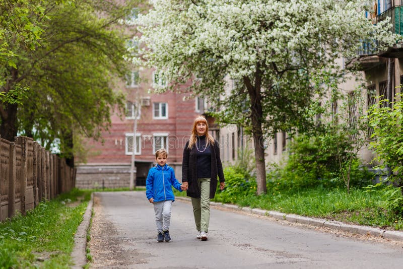 A woman of fifty walks by the hand with her seven-year-old grandson in the city quarter in the spring, blooming Apple trees royalty free stock photo A woman of fifty walks by the hand with her seven-year-old grandson in the city quarter in the spring, blooming Apple trees royalty free stock photo