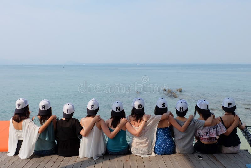 Women friends sit hug together with FRIENDSHIP Cap blue sea sky