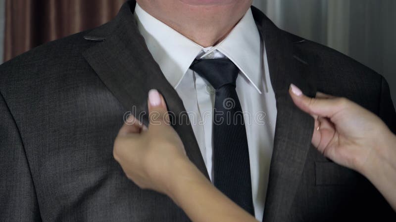 Women hands correct and tighten tie knot on man neck and stroking his jacket